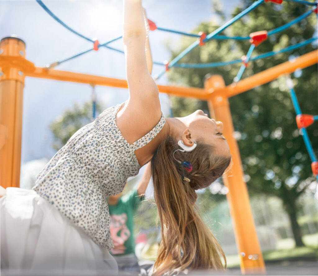 Ein kleines Mädchen mit einem Cochlea Implantat spielt auf einem Spielplatz in einem Klettergerät